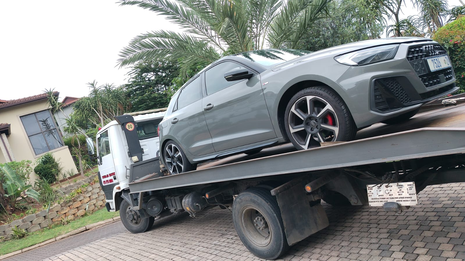 Grey Audi A1 on a flatbed in a residential driveway