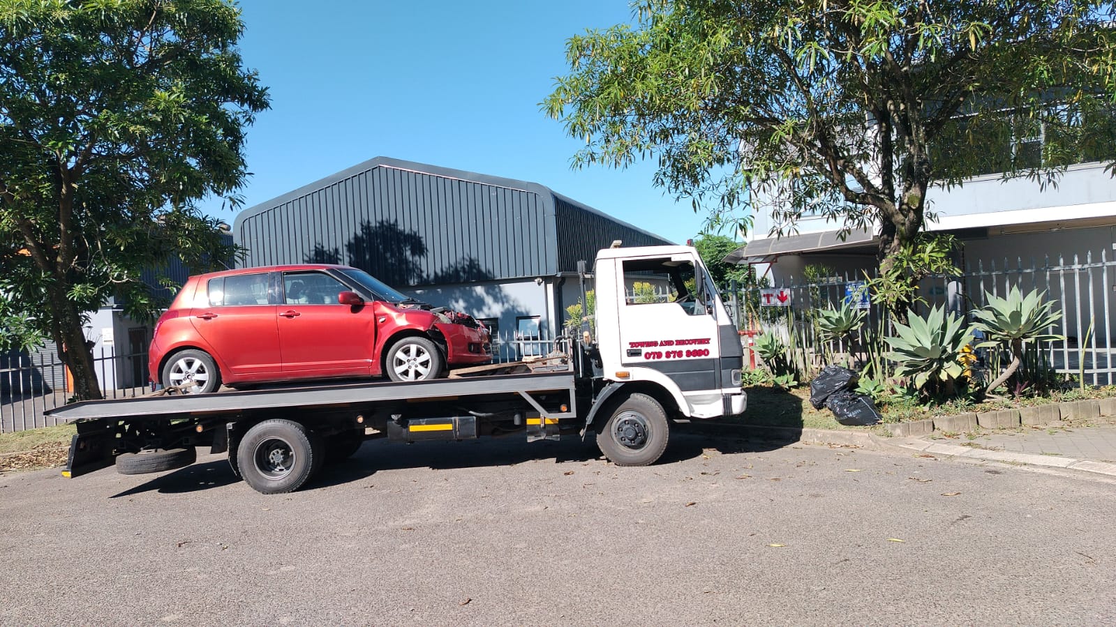Red Suzuki Swift with front damage on a flatbed tow truck